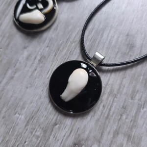 Puede incluir: Un collar con colgante negro con un dije blanco en forma de diente. El dije est&aacute; sobre un fondo negro dentro de un bisel plateado. El collar tiene un cord&oacute;n negro.