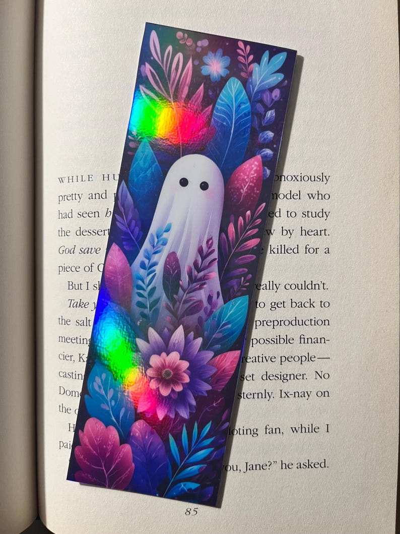 Op de afbeelding: Rechthoekige boekenlegger met een witte geest omringd door kleurrijke bladeren en bloemen. De boekenlegger heeft een holografisch regenboogeffect. Het nummer 85 is zichtbaar aan de onderkant.