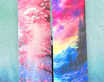 May include: Two bookmarks with a galaxy theme. The left bookmark features a pink and purple sky with a cherry blossom tree. The right bookmark features a blue and purple sky with a mountain range and a river.