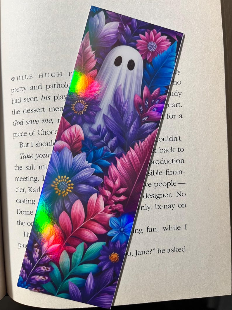 Op de afbeelding: Rechthoekige boekenlegger met een wit spookontwerp, tegen een achtergrond van paarse, roze en blauwe bloemen en bladeren. De boekenlegger heeft een holografisch effect en is bedoeld voor boeken.