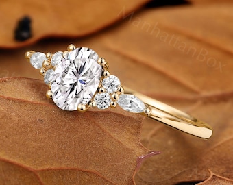 May include: A gold ring featuring a central oval-cut white gemstone flanked by two smaller round-cut stones and one marquise-cut stone on each side. The band is polished yellow gold, showcasing a multi-stone cluster design with clear, faceted stones.