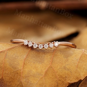 Puede incluir: Una delicada banda de boda curvada de oro rosa con una fila de pequeños diamantes transparentes.