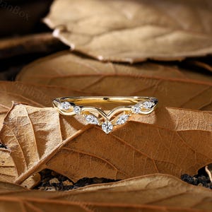 K&ouml;nnte beinhalten: Ein zarter goldener Ehering mit einem V-f&ouml;rmigen Design und kleinen Diamanten, die in die Band eingefasst sind.
