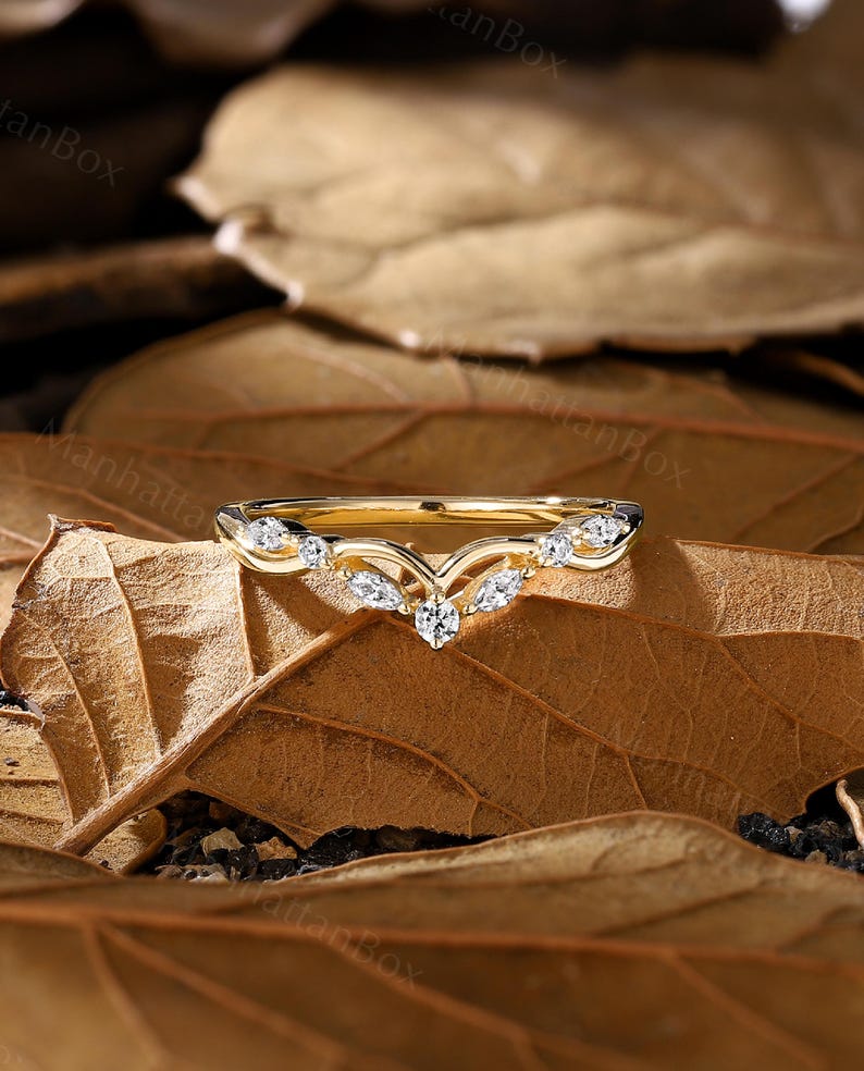 K&ouml;nnte beinhalten: Ein zarter goldener Ehering mit einem V-f&ouml;rmigen Design und kleinen Diamanten, die in die Band eingefasst sind.
