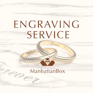 Könnte beinhalten: Zwei goldene Eheringe mit Diamantbesatz, graviert mit dem Wort "Forever". Die Ringe liegen auf einem weißen Holzgrund mit dem Text "Engraving Service" und "ManhattanBox".