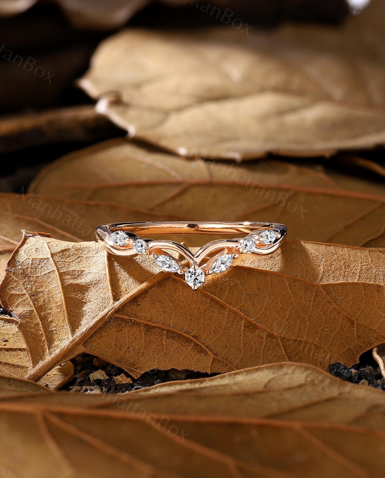 May include: A rose gold wedding band with a v-shaped design and small diamonds set in the band.