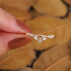 K&ouml;nnte beinhalten: Ein zarter Ring aus Ros&eacute;gold mit einem geschwungenen Design, das mit kleinen, klaren Edelsteinen besetzt ist. Der Ring ist mit einem Steincluster in der Mitte besetzt, was einen einzigartigen und eleganten Look erzeugt.