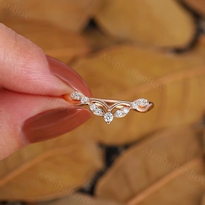 K&ouml;nnte beinhalten: Ein zarter Ring aus Ros&eacute;gold mit einem geschwungenen Design, das mit einer Reihe kleiner Diamanten besetzt ist. Der Ring ist mit einem gr&ouml;&szlig;eren Diamanten in der Mitte besetzt.