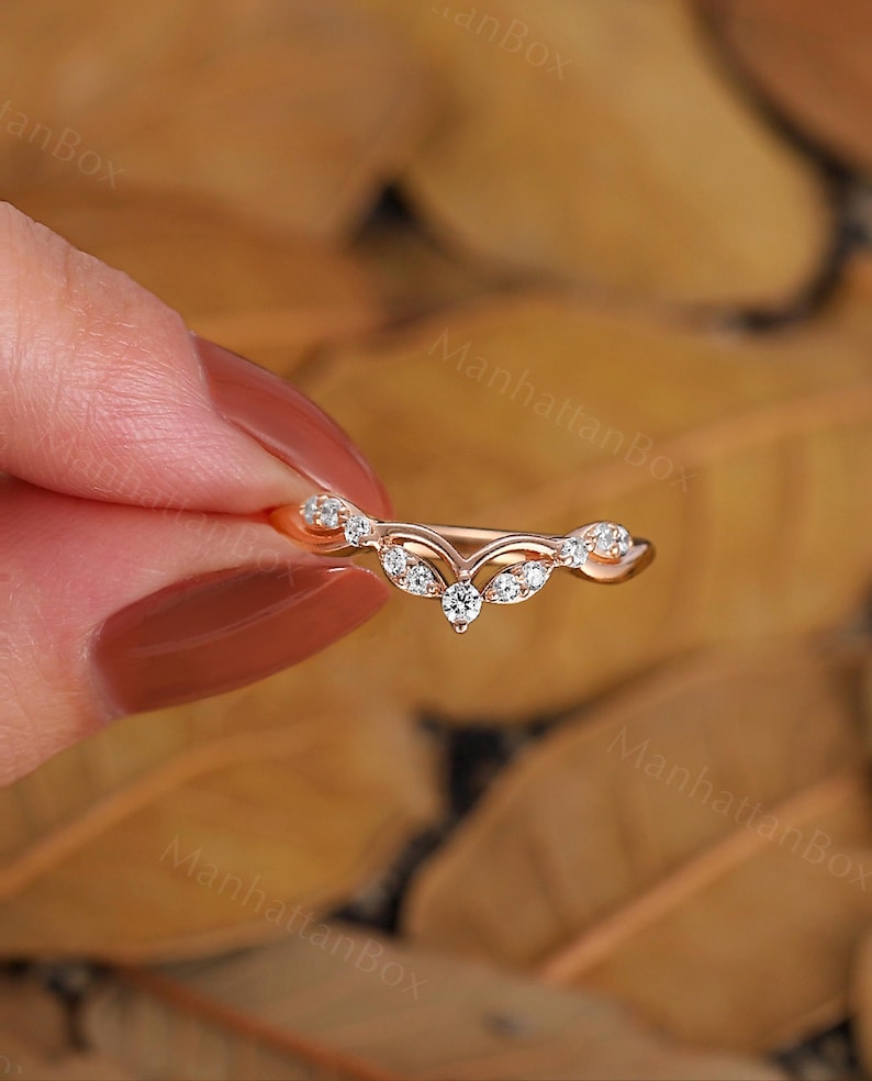 K&ouml;nnte beinhalten: Ein zarter Ring aus Ros&eacute;gold mit einem geschwungenen Design, das mit einer Reihe kleiner Diamanten besetzt ist. Der Ring ist mit einem gr&ouml;&szlig;eren Diamanten in der Mitte besetzt.