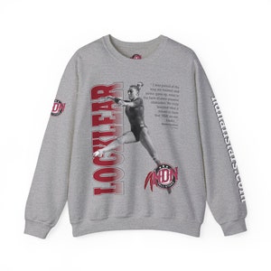 Puede incluir: Sudadera gris con un gráfico rojo y blanco de una gimnasta en el aire. El gráfico incluye el texto "LOCKLEAR" y "AND1N ALL-STARS". La cita "Estaba orgulloso de la forma en que entrenamos y nunca nos dimos por vencidos, incluso frente a obstáculos omnipresentes. Realmente aprendimos lo que significaba tener esa "USA" en nuestras espaldas." está impresa en la sudadera.