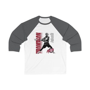 May include: A white and grey baseball t-shirt with a red and white graphic of a lacrosse player. The graphic includes the text "Thompson" and a quote: "Whether you're big or small, fast or slow, everyone encounters adversity. Find your inner strength and tell that adversity to shut up."