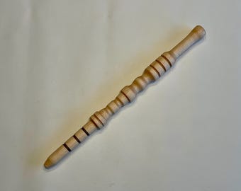 Peut inclure: Une baguette en bois de couleur claire avec une poignée arrondie et une extrémité effilée. La baguette présente une série d'anneaux sculptés et un motif texturé et nervuré sur toute sa longueur. La baguette mesure environ 25 cm de long.