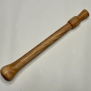 May include: A wooden recorder, a musical instrument, is shown against a white backdrop. The recorder is made of light brown wood, with a cylindrical body and flared ends. The instrument is approximately 30 cm long.
