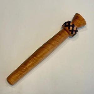 Könnte beinhalten: Ein Nudelholz aus Holz mit hellbraunem Finish und einem dekorativen schwarzen Lederband. Das Nudelholz hat ein konisches Design und einen ausgestellten Griff. Die Holzmaserung ist sichtbar.