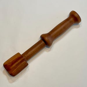 May include: A wooden muddler, featuring a cylindrical handle and a ridged, rectangular head. The light brown wood muddler is designed for mixing ingredients in cocktails and other drinks. The muddler measures approximately 20 cm in length.