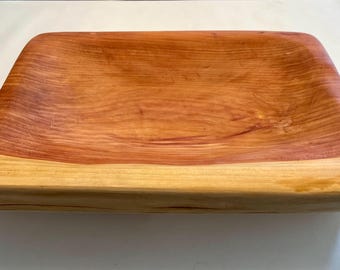 Könnte beinhalten: Ein rechteckiges Serviertablett aus Holz mit natürlicher Maserung. Das Tablett hat einen rotbraunen Innenraum und einen helleren, gelblich-braunen Rand. Die Holzmaserung ist im gesamten Tablett sichtbar.