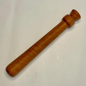 Può includere: Un mattarello in legno marrone chiaro. Il mattarello ha un corpo cilindrico con estremità arrotondate e un'impugnatura decorativa. La venatura del legno è visibile, aggiungendo alla sua estetica naturale. Questo utensile da cucina è progettato per stendere l'impasto.