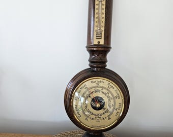 Può includere: Una stazione meteorologica da parete in legno scuro dotata di un termometro verticale nella parte superiore, un grande barometro centrale con quadrante dorato marchiato Baromaster e un piccolo igrometro circolare nella parte inferiore.