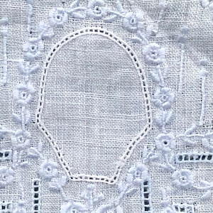 May include: White linen fabric with a delicate embroidered design featuring a floral motif and a circular frame. The embroidery is done in a light blue thread.
