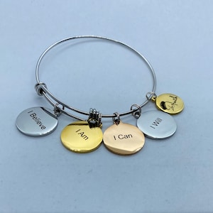Puede incluir: Una pulsera de alambre extensible en tono plateado con cinco dijes circulares en tonos plata, oro y oro rosa. Los dijes están grabados con las frases I Believe, I Am, I Can, I Will y un logotipo en letra cursiva.