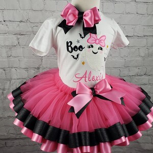 May include: Pink and black tutu with a pink bow and a white shirt with a ghost and the text "Boo Alexis".