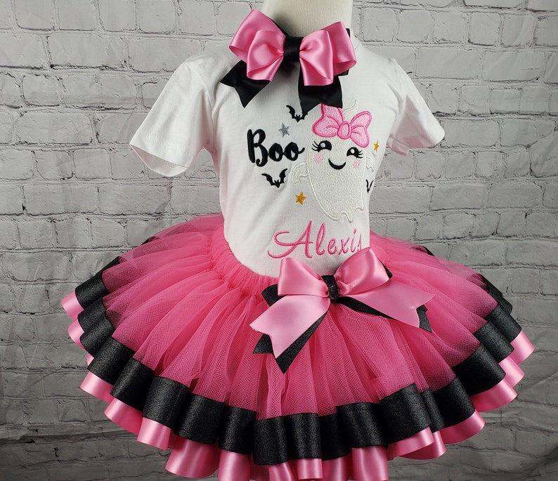 May include: Pink and black tutu with a pink bow and a white shirt with a ghost and the text "Boo Alexis".