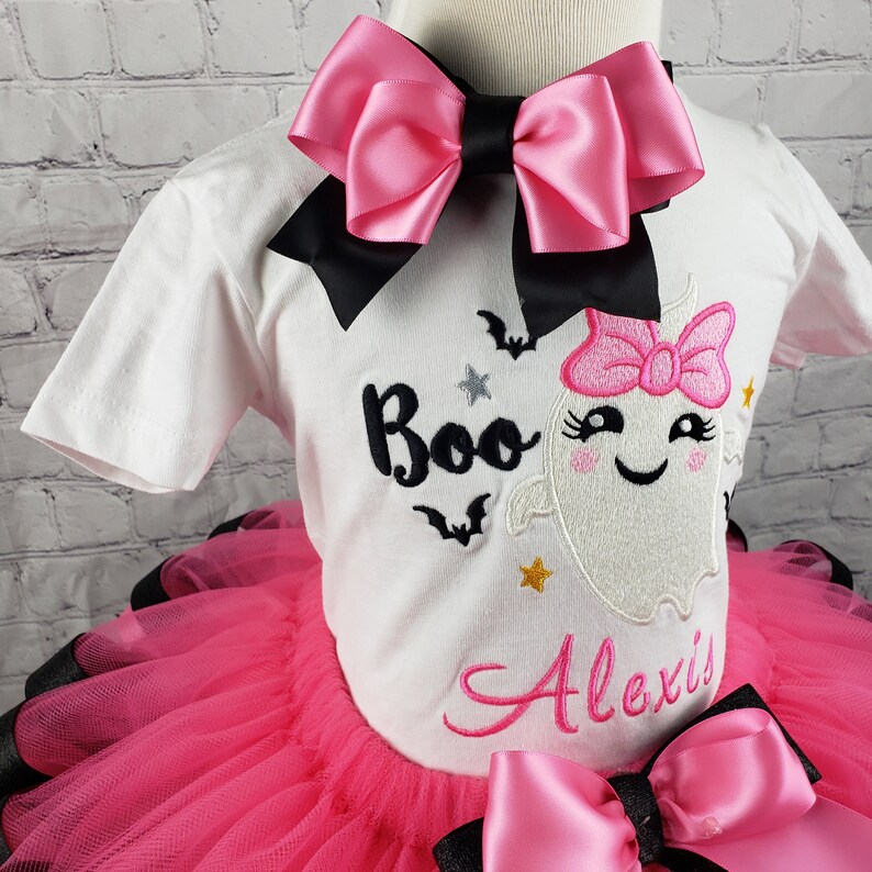 May include: A pink and black tutu with a white shirt featuring a ghost with a pink bow and the text "Boo" and "Alexis".