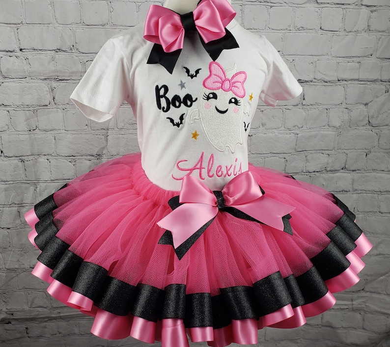 May include: A pink and black tutu with a white shirt featuring a ghost with a pink bow and the text "Boo" and "Alexis".