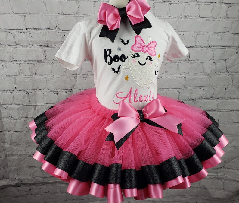 May include: A pink and black tutu with a white shirt featuring a ghost with the text "Boo" and the name "Alexis".
