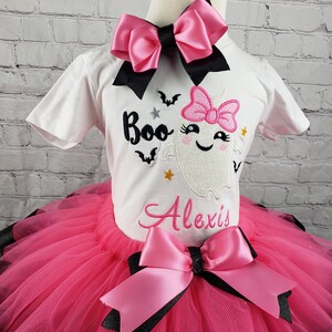 May include: A pink and black tutu with a white shirt featuring a ghost with a pink bow and the text "Boo Alexis".