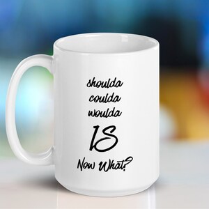 May include: White ceramic coffee mug with black text that reads "shoulda coulda woulda 18 Now What?"