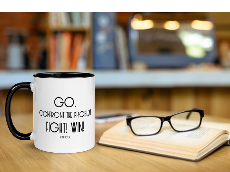 May include: White coffee mug with a black rim and handle. The mug has black text that reads "GO. CONFRONT THE PROBLEM FIGHT! WIN! EDNA MODE".