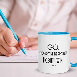 May include: White ceramic coffee mug with a blue rim and handle. The mug has black text that reads "GO. CONFRONT THE PROBLEM. FIGHT! WIN!" with the words "ZEN MODE" in smaller text below.