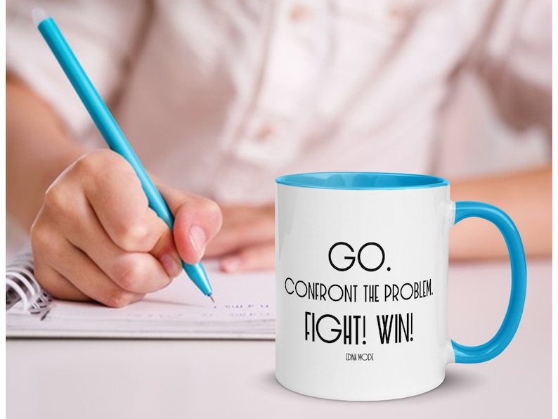 May include: White ceramic coffee mug with a blue rim and handle. The mug has black text that reads "GO. CONFRONT THE PROBLEM. FIGHT! WIN!" with the words "ZEN MODE" in smaller text below.