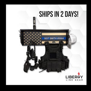 May include: A black tactical vest and accessories are displayed below a wooden shelf with an American flag design. The shelf includes a blue line with the text "SGT SMITH #5664". A flashlight and a white helmet are also visible.