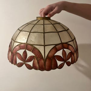 May include: A vintage lampshade with a domed shape. The shade features a geometric pattern of off-white and reddish-brown segments, with a decorative floral design at the bottom. The frame is a gold colour.