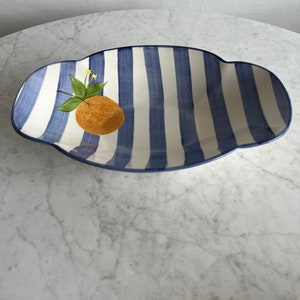 May include: An oval serving dish with white and blue stripes and a painted orange and green leaves.