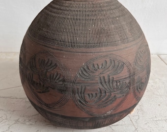 Op de afbeelding: Een grote, ronde, bruine keramische vaas met een getextureerd oppervlak en gegraveerde ontwerpen. De vaas heeft een brede opening aan de bovenkant en een smalle basis.