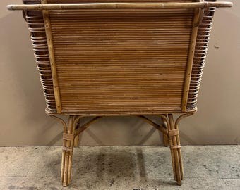 May include: A rectangular, woven rattan planter with a top rail and four legs. The planter is made of natural brown rattan.