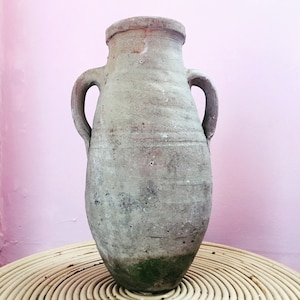 May include: A large, gray, earthenware jug with two handles. The jug has a rough, textured surface and appears to be very old.