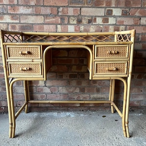 May include: A vintage bamboo desk with four drawers and a woven design. The desk has a light brown color and a glass top. The drawers have wooden handles. The desk is supported by curved legs.