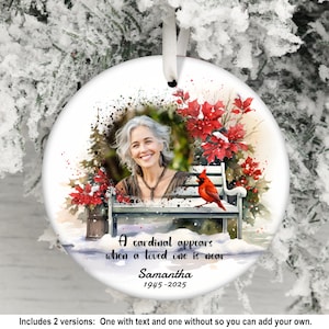 May include: A round ceramic ornament featuring a photo of a smiling woman, surrounded by a watercolor scene of red poinsettias, a bench, and a red cardinal. Text reads "A cardinal appears when a loved one is near" and "Samantha 1945-2025".
