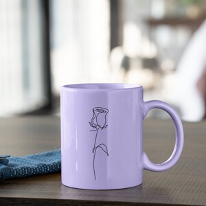 May include: A lavender ceramic mug with a single line drawing of a rose on the front.