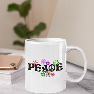 May include: White ceramic mug with a black "PEACE" graphic and colorful flower designs. The mug has a white handle.