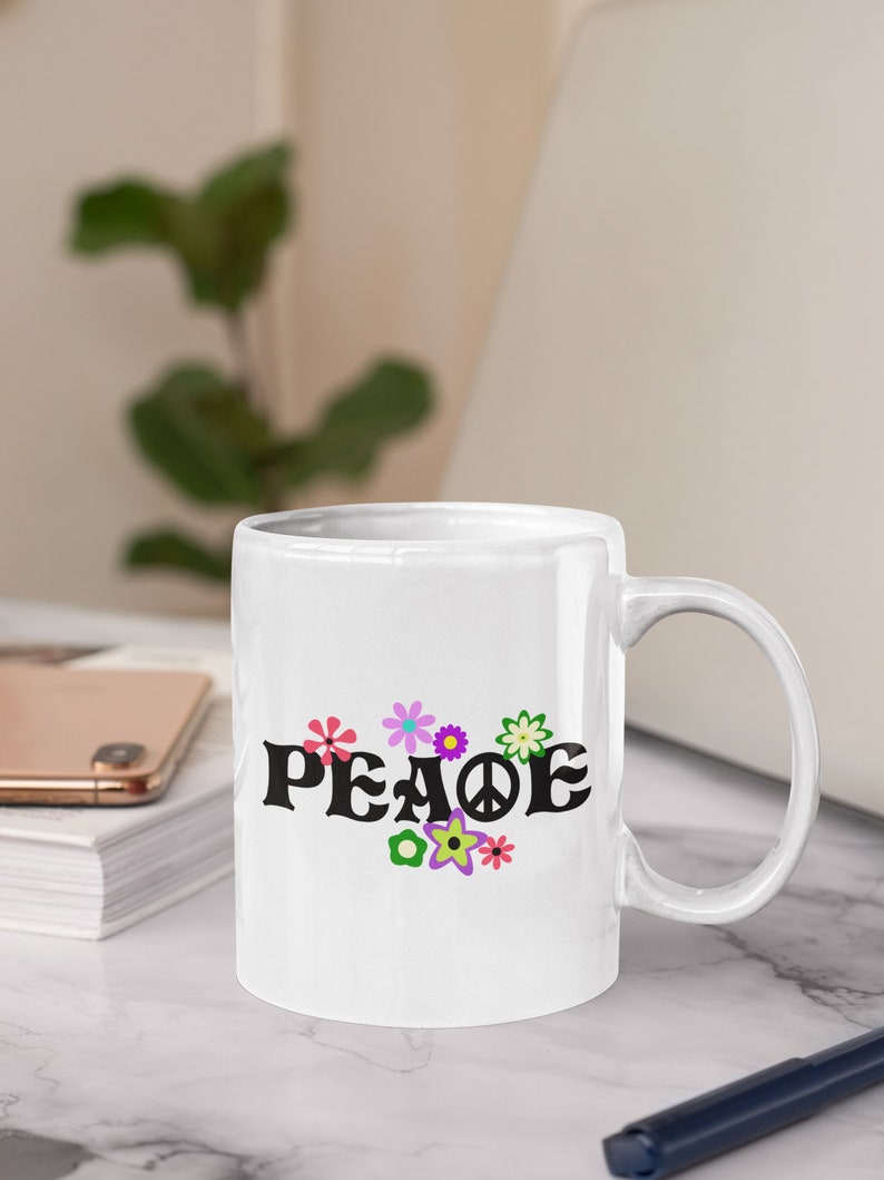 May include: White ceramic mug with a black "PEACE" graphic and colorful flower designs. The mug has a white handle.