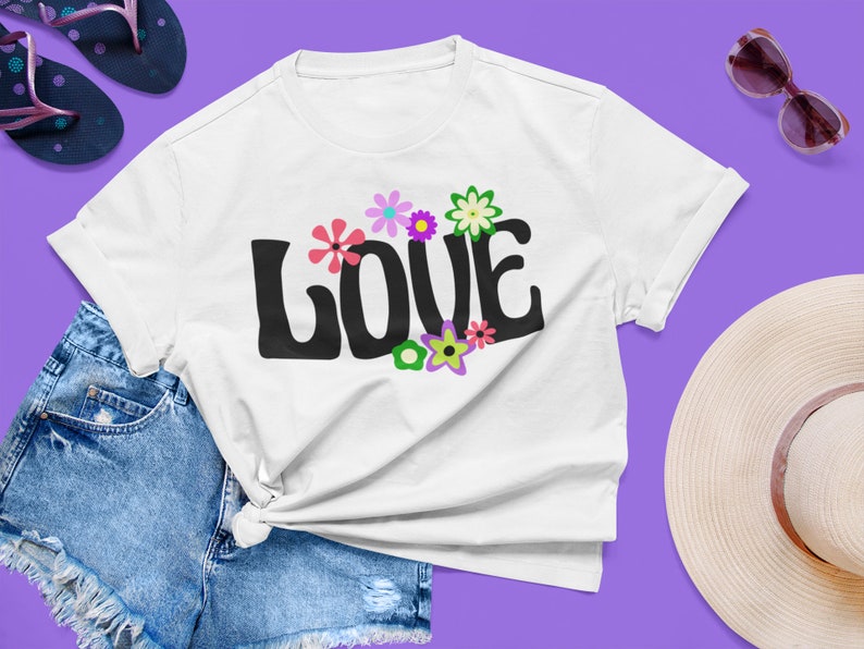 May include: White t-shirt with a black "LOVE" graphic in a retro font. The graphic is surrounded by colorful flowers with pink, purple, green, and yellow petals.