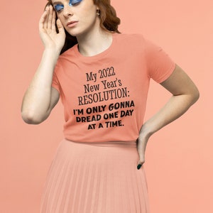 May include: A peach-colored t-shirt with black text that reads "My 2022 New Year's RESOLUTION: I'M ONLY GONNA DREAD ONE DAY AT A TIME."