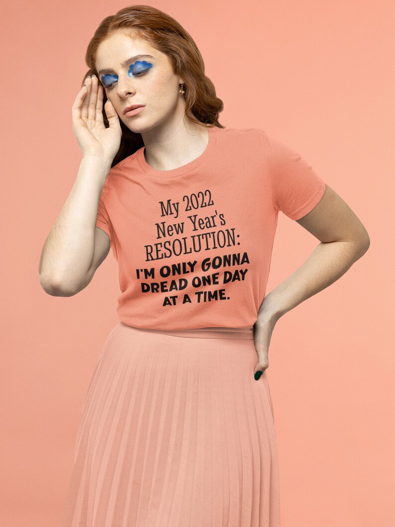 May include: A peach-colored t-shirt with black text that reads "My 2022 New Year's RESOLUTION: I'M ONLY GONNA DREAD ONE DAY AT A TIME."