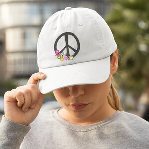 May include: White baseball cap with a black peace sign and colorful flowers embroidered on the front.