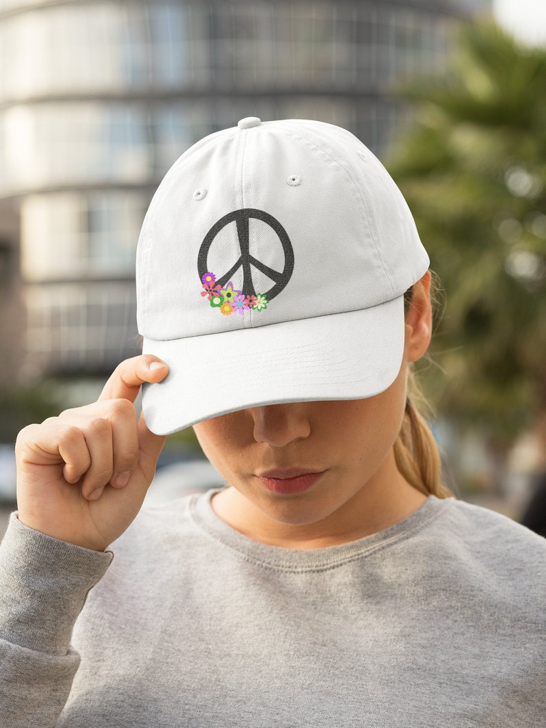 May include: White baseball cap with a black peace sign and colorful flowers embroidered on the front.